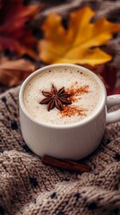 A cozy cup of warm spiced latte topped with a beautiful star anise and a sprinkle of cinnamon, surrounded by autumn leaves and a knitted blanket, evoking comfort and warmth.