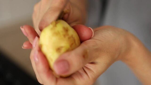 A person demonstrates the simple process of peeling a potato. Holding a knife, they expertly remove the skin while preparing for cooking. female hands peeling potatoes