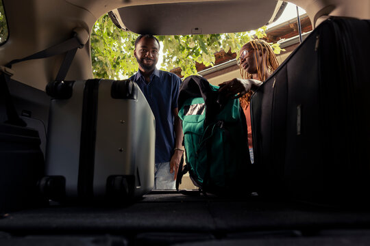 African american joyful people preparing their automobile for a road trip, packing the car trunk in anticipation of a relaxing summer journey. Cute boyfriend and girlfriend on romantic getaway.