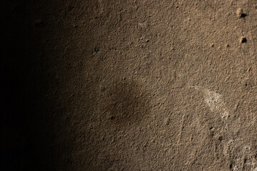 A close-up, macro shot of a rough, earthy concrete or stone texture, illuminated by dramatic side-light that fades into a deep black shadow. A perfect rustic, grunge, and abstract background.