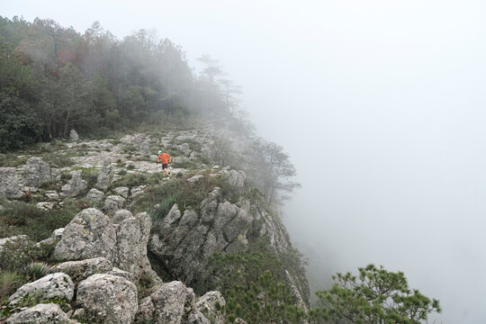 One man running on a rocky trail at high mountain during a foggy day.