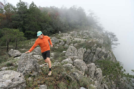 One man running on a rocky trail at high mountain during a foggy day.