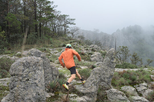 One man from behind running on a high rocky mountain at a foggy day