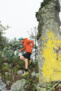 One man running in the mountain next to a rock with yellow liquen