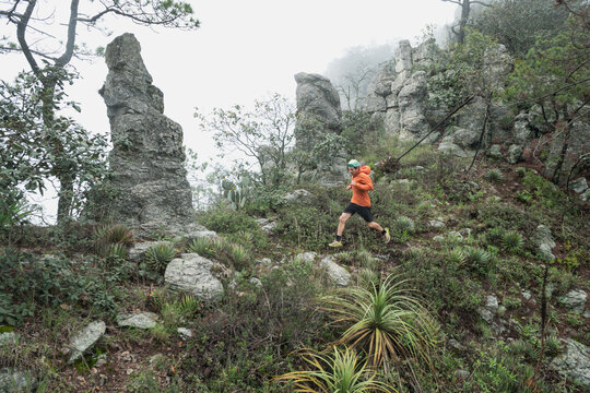 One man running on a trail next to high rocks during a foggy day.