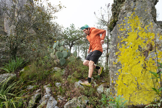 One man running in the mountain next to a rock with yellow liquen