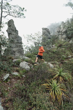 One man running on a trail next to high rocks during a foggy day.