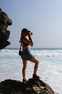 Woman with camera standing on rock by ocean