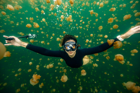 woman diving through jellyfish at isolated lake in Raja Ampat