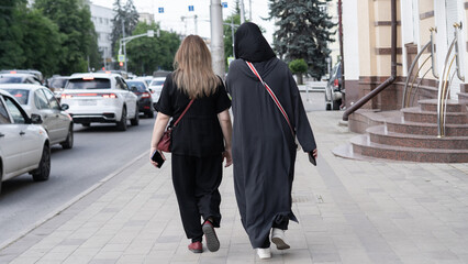 Two women walking on a city street wearing contrasting clothing styles during the afternoon
