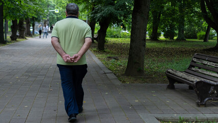 Man walks alone in park with hands clasped behind back on a serene day in a green setting