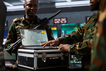 Military officer looking at surveillance footage on laptop, analyzing data to allocate resources to...