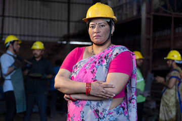 Portrait of beautiful young woman in hardhat confidently at camera enjoying work in modern factory
