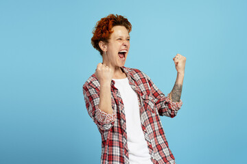 Excited young woman with piercing reacting to win, screaming, isolated on blue background