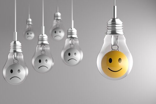 Single yellow happy light bulb among sad white light bulbs hanging from the ceiling