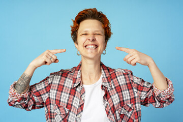 Young woman pointing index fingers on opened mouth teeth isolated on blue background