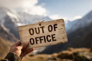 Scenic mountain view with hand holding wooden sign stating Out of Office during a peaceful outdoor retreat