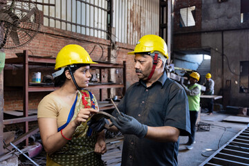 Two indian engineers wearing safety hard hat and discussing work at industrial factory, skill india...