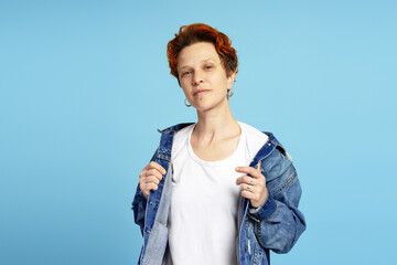 Portrait of stylish individual woman posing in denim jacket, isolated on blue background