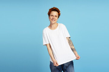 Cheerful woman with short red hair and tattoos on arms, wearing white t shirt and blue jeans
