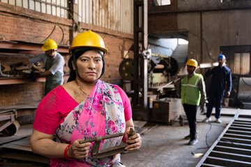 Portrait of beautiful young woman in hardhat confidently at camera enjoying work in modern factory