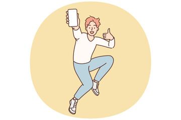 Encouraged man jumps up with mobile phone in hands showing blank screen gadget and shows thumbs up