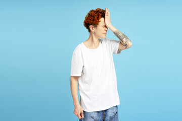 Portrait of desperate woman with piercing and tattoo putting hand on head in studio