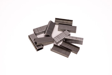A macro close-up of metal staples stacked on a clean white background. The sharp edges, smooth...