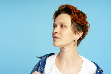 Portrait of trendy red-haired young woman with facial piercings, posing in studio