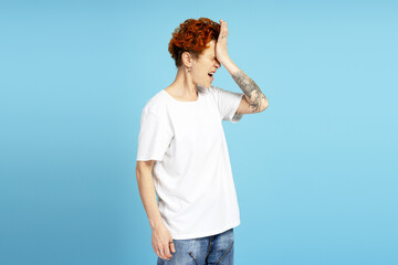 Portrait of upset woman with piercing and tattoo putting hand on head over blue background