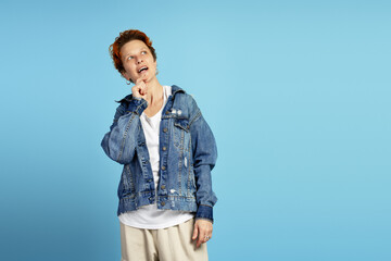Thoughtful stylish woman thinking, wearing in denim jacket on blue background looking on copy space