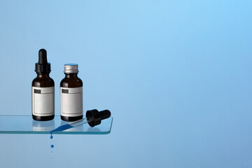 Amber glass serum bottles with dropper and drops on the bath shelf at blue background. Perfect representation of modern skincare, beauty rituals, and cosmetic treatments. Copy space