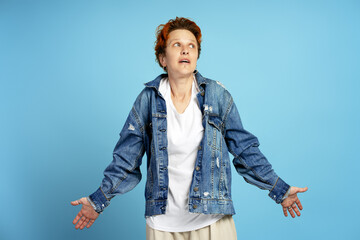 Surprised young woman with short red hair in denim jacket posing on blue background