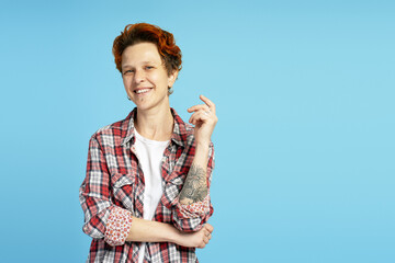 Smiling young woman with short red hair and piercings posing on blue background in studio