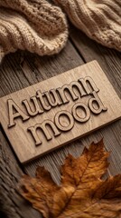 A warm autumn scene captures a wooden sign displaying 'Autumn Mood' alongside beautifully arranged leaves resting on textured fabric, evoking feelings of comfort and nostalgia.