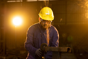 Mechanic using circular saw grinder tool with protective work wear at factory.