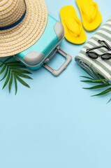 Suitcase, beach towel, flip flops, sunglasses and a straw hat suggesting summer vacation travel