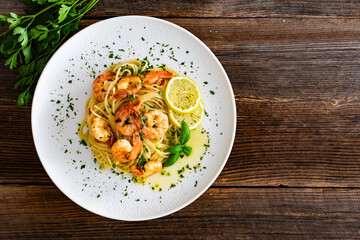 Spaghetti with fried shrimps, olive oil and parsley on wooden table