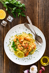 Spaghetti with fried shrimps, olive oil and parsley on wooden table