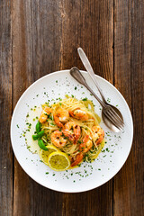 Spaghetti with fried shrimps, olive oil and parsley on wooden table