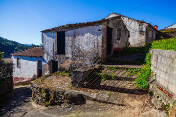 A weathered, white-washed house with a tiled roof stands on a quiet street