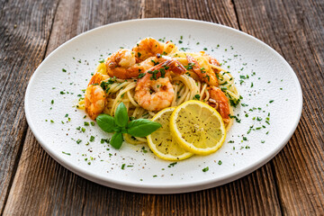 Spaghetti with fried shrimps, olive oil and parsley on wooden table
