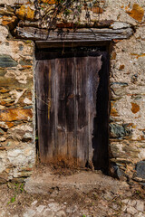 Fototapeta premium A weathered wooden door set in a stone wall stands under sunlight