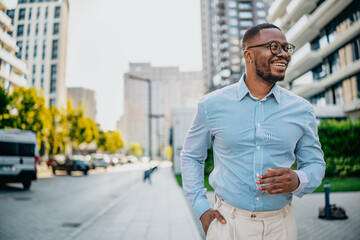 Businessman in modern urban setting smiling while walking near tall buildings during daylight hours