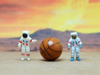 Mini toy of action figure with blurred background. Miniature diorama photography concept design. Minifigure of Astronaut character at space with ball. Sportsman playing basketball at moon.