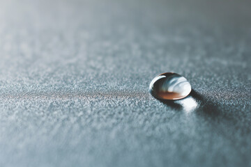 macro shot of water droplet on matte metal surface emphasizing interplay of light and texture