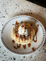 Fluffy pancakes topped with vanilla ice cream, chocolate flakes, and caramel drizzle, served on a ceramic plate—perfect for breakfast or dessert inspiration.