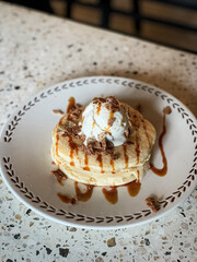 Fluffy pancakes topped with vanilla ice cream, chocolate flakes, and caramel drizzle, served on a ceramic plate—perfect for breakfast or dessert inspiration.