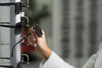 Close-up of hands of a young woman who chooses sunglasses on the showcase for purchase in an optical store. Optometry, eyesight, eyeglasses, accessories, fashion, lifestyle