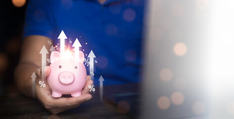 Savings and financial planning concept. Man using laptop and holding piggy bank on wooden table. Income, return, retirement, provident fund, investment, dividend tax, stock market.